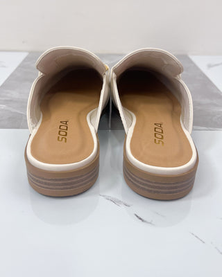 Pair of white sandals with brown soles on a light gray surface