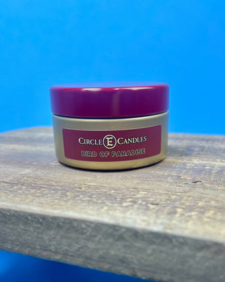 Bird of Paradise tropical scented candle in a brushed gold travel tin with a berry-colored lid, featuring a clean-burning single wick and available in multiple sizes for home fragrance.