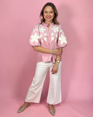 Woman wearing a pink floral blouse and white pants against a pink background