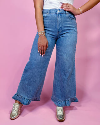 Person wearing blue wide-leg jeans with ruffled hem on a pink background
