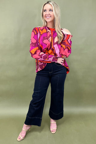 Woman wearing a colorful patterned blouse and dark jeans on a green background
