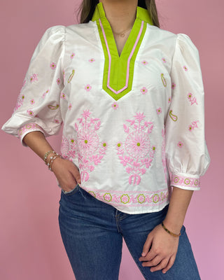 Woman wearing a white blouse with pink floral patterns and green accents against a pink background