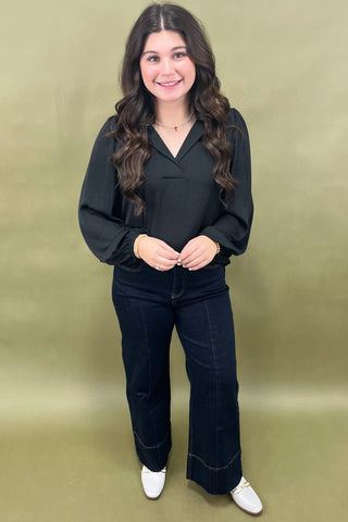 Woman wearing a black outfit with white shoes against a green background