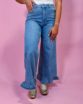 Person wearing blue jeans with ruffled cuffs on a pink background