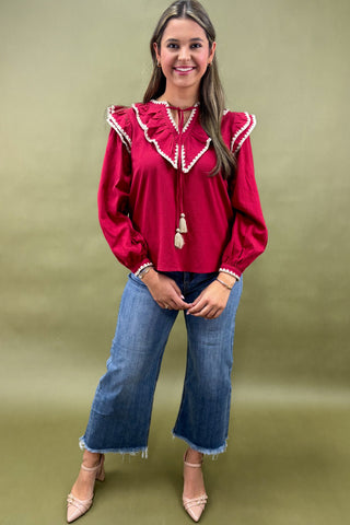 Woman wearing a red blouse with white trim and blue jeans on a green background