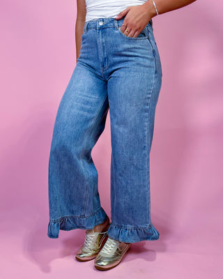 Person wearing blue jeans with ruffled cuffs on a pink background