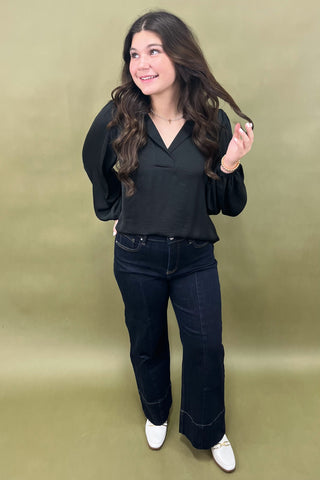 Woman wearing a black blouse and dark jeans against a green background