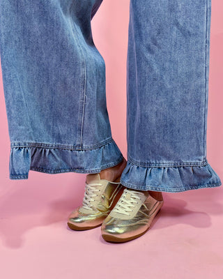 Gold sneakers worn with blue jeans on a pink background
