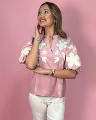 Woman wearing a pink blouse with white floral patterns against a pink background