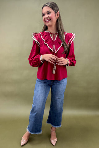 Woman wearing a red blouse with white ruffles and blue jeans against a green background