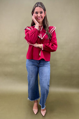 Woman wearing a red blouse with white trim and blue jeans on a beige background