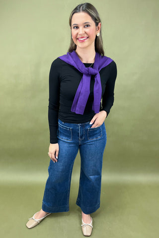 Woman wearing a black top, blue jeans, and a purple scarf on a green background