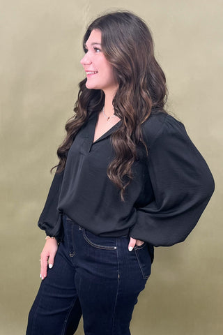 Woman wearing a black blouse and dark jeans against a beige background
