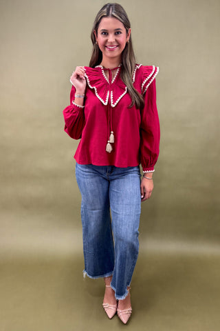 Woman wearing a red blouse with white trim and blue jeans on a beige background