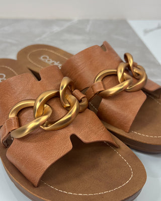 Brown sandals with gold chain details on a light gray surface
