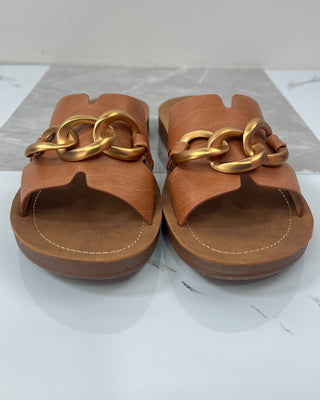 Pair of brown sandals with gold chain details on a light background