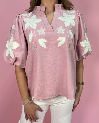 Pink blouse with white floral embroidery on a pink background