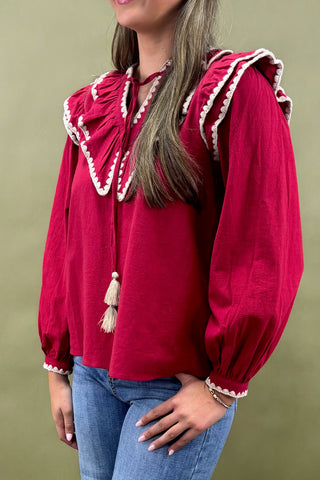 Red blouse with ruffled collar and tassels worn by a person on a green background