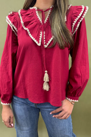 Red blouse with white trim and tassels worn by a person on a green background