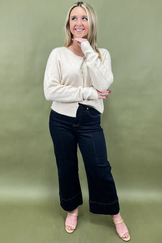 Woman wearing a white sweater and black pants against a green background