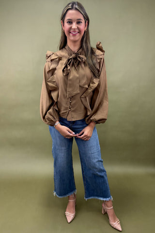 Woman wearing a brown blouse with ruffled details and blue jeans on a green background