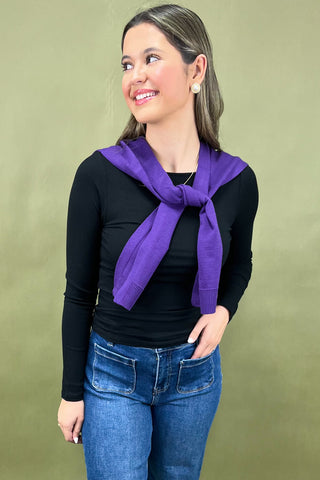 Woman wearing a purple scarf, black top, and blue jeans against a green background