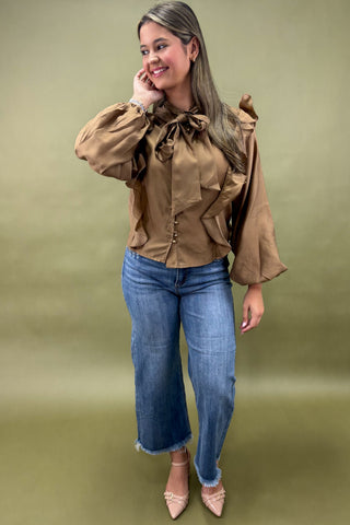 Woman wearing a brown blouse with ruffled details and blue jeans on a green background