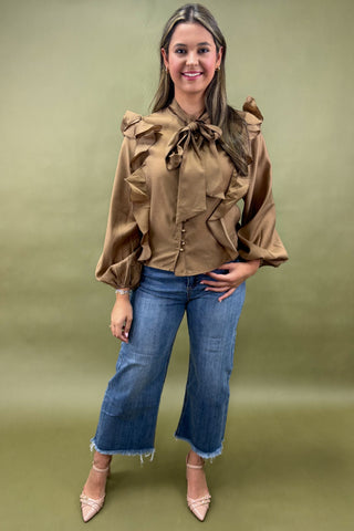 Woman wearing a brown blouse with ruffles and blue jeans on a green background