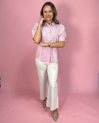 Woman wearing a pink striped shirt and white pants against a pink background