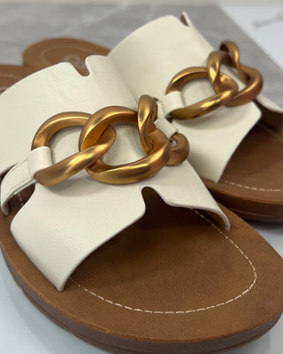 Beige sandals with gold chain detail on a white background