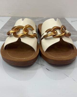 Pair of white sandals with gold chain design on a light gray background