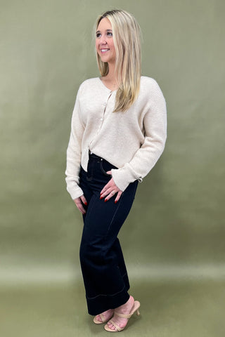 Woman wearing a cream cardigan and dark pants against a green background