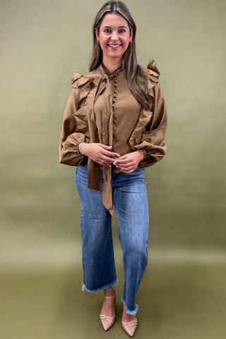 Woman wearing a brown blouse and blue jeans against a green background