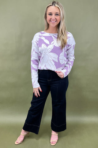 Woman wearing a purple floral sweater and black pants against a green background