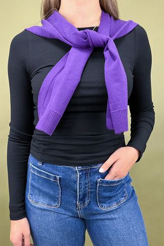 Person wearing a purple scarf, black long-sleeve top, and blue jeans on a beige background