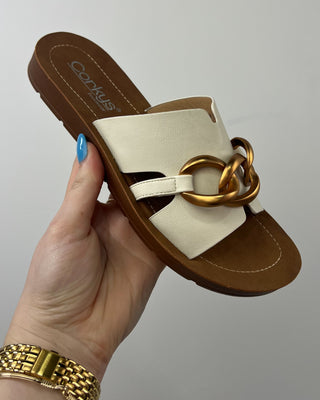 Beige sandal with gold chain detail held by a hand against a neutral background