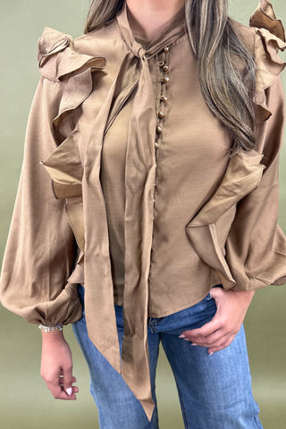 Brown blouse with ruffled sleeves worn by a person on a green background