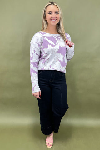 Woman wearing a purple floral sweater and black pants against a green background