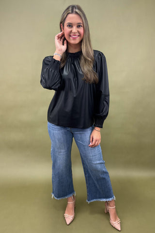 Woman wearing a black blouse and blue jeans against a green background