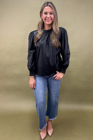 Woman wearing a black blouse and blue jeans against a beige background