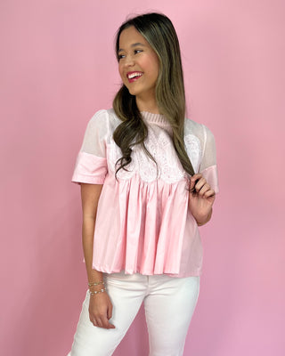 Woman wearing a pink blouse with lace details against a pink background