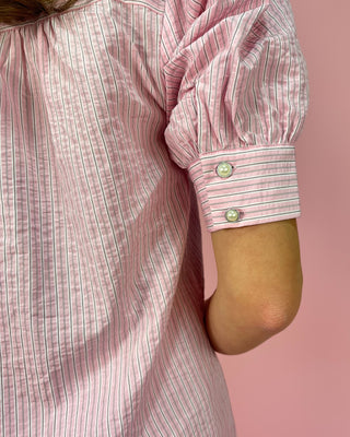 Close-up of a person wearing a pink striped shirt with rolled-up sleeves against a pink background