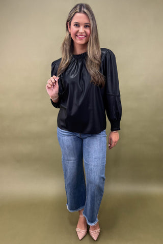 Woman wearing a black blouse and blue jeans against a beige background