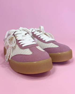 Purple sneakers with white laces and brown soles on a pink background