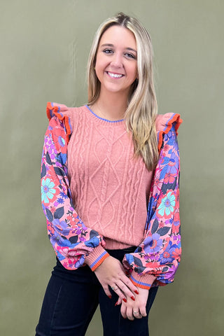 Woman wearing a pink sweater with colorful floral sleeves against a green background