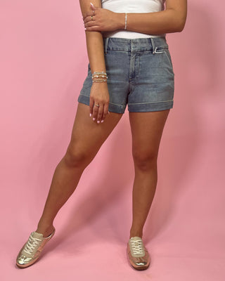 Person wearing denim shorts and gold sneakers on a pink background