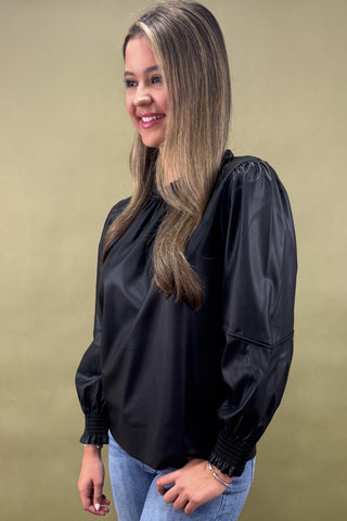 Woman wearing a black blouse with balloon sleeves against a beige background