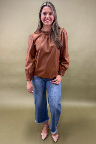 Woman wearing a brown blouse and blue jeans against a beige background