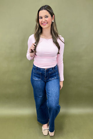Woman wearing a pink top and blue jeans against a green background