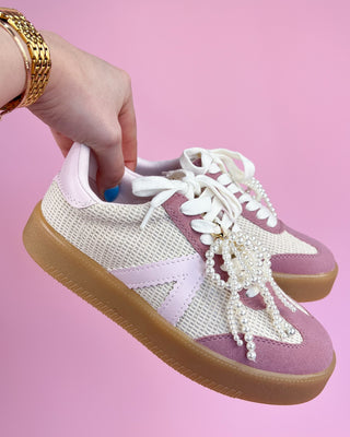 Pink and white sneaker with pearl details held by a hand against a pink background